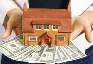 A person holding a miniature house and some dollar bills